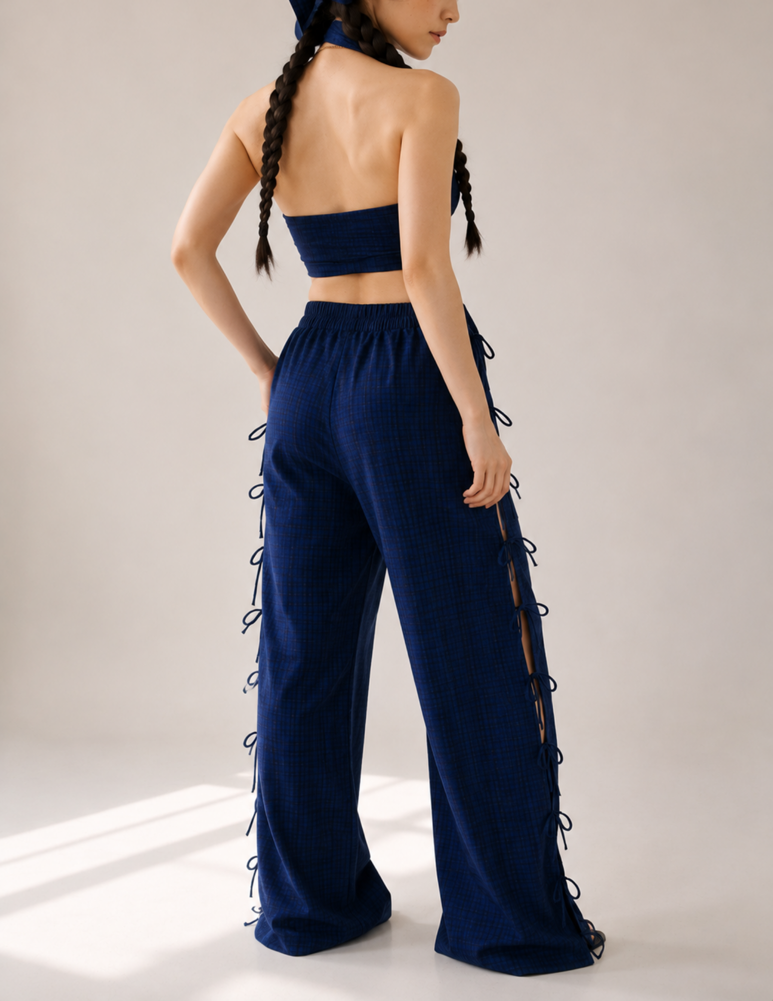 A model shown from the back wearing a matching navy blue two-piece set consisting of a strapless bandeau top and high-waisted wide-leg pants with lace-up side details, set against a neutral studio background.