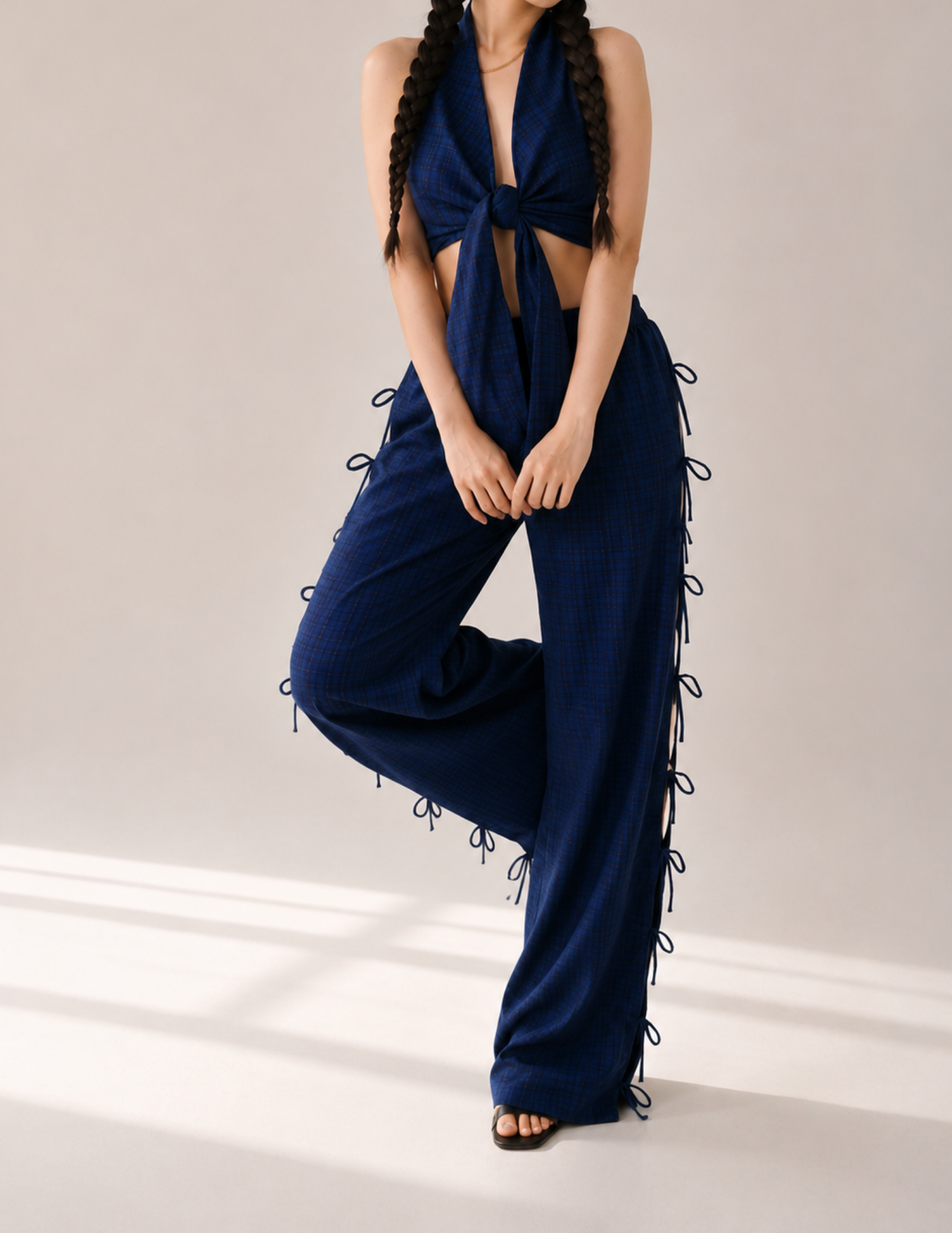 A model wearing a navy blue halter jumpsuit with a front twist detail and side lace-up ties, posed against a neutral studio background.