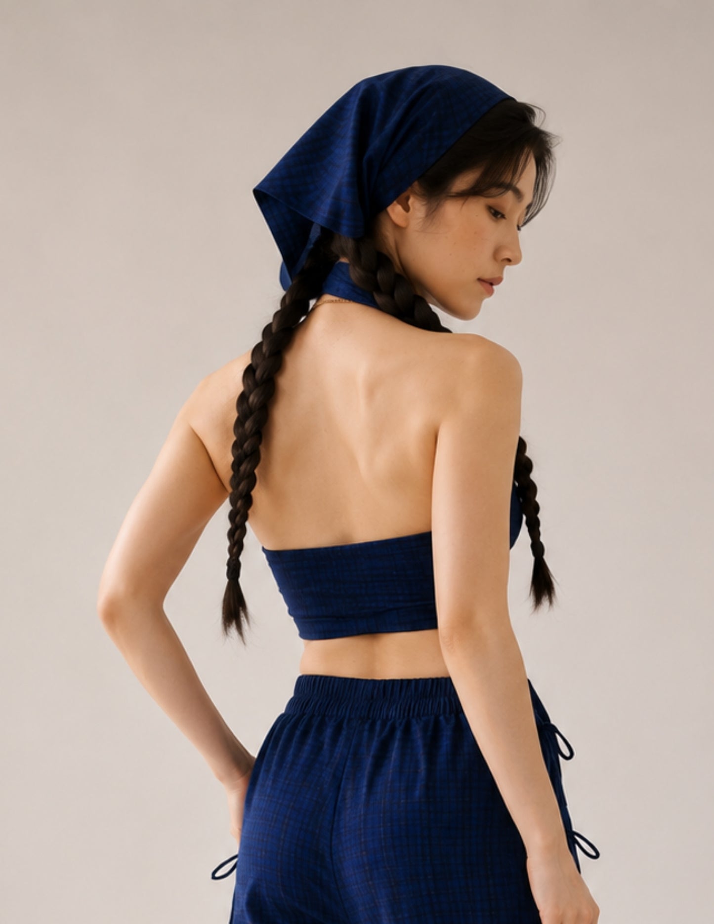 A woman shown from the back wearing a matching navy blue set consisting of a halter crop top, high-waisted drawstring pants, and a matching headscarf, set against a plain light gray studio background.