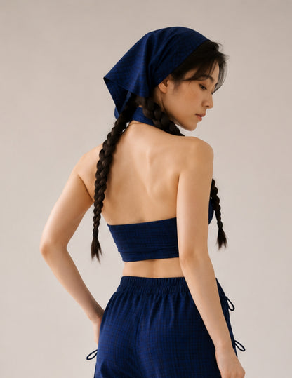 A woman shown from the back wearing a matching navy blue set consisting of a halter crop top, high-waisted drawstring pants, and a matching headscarf, set against a plain light gray studio background.