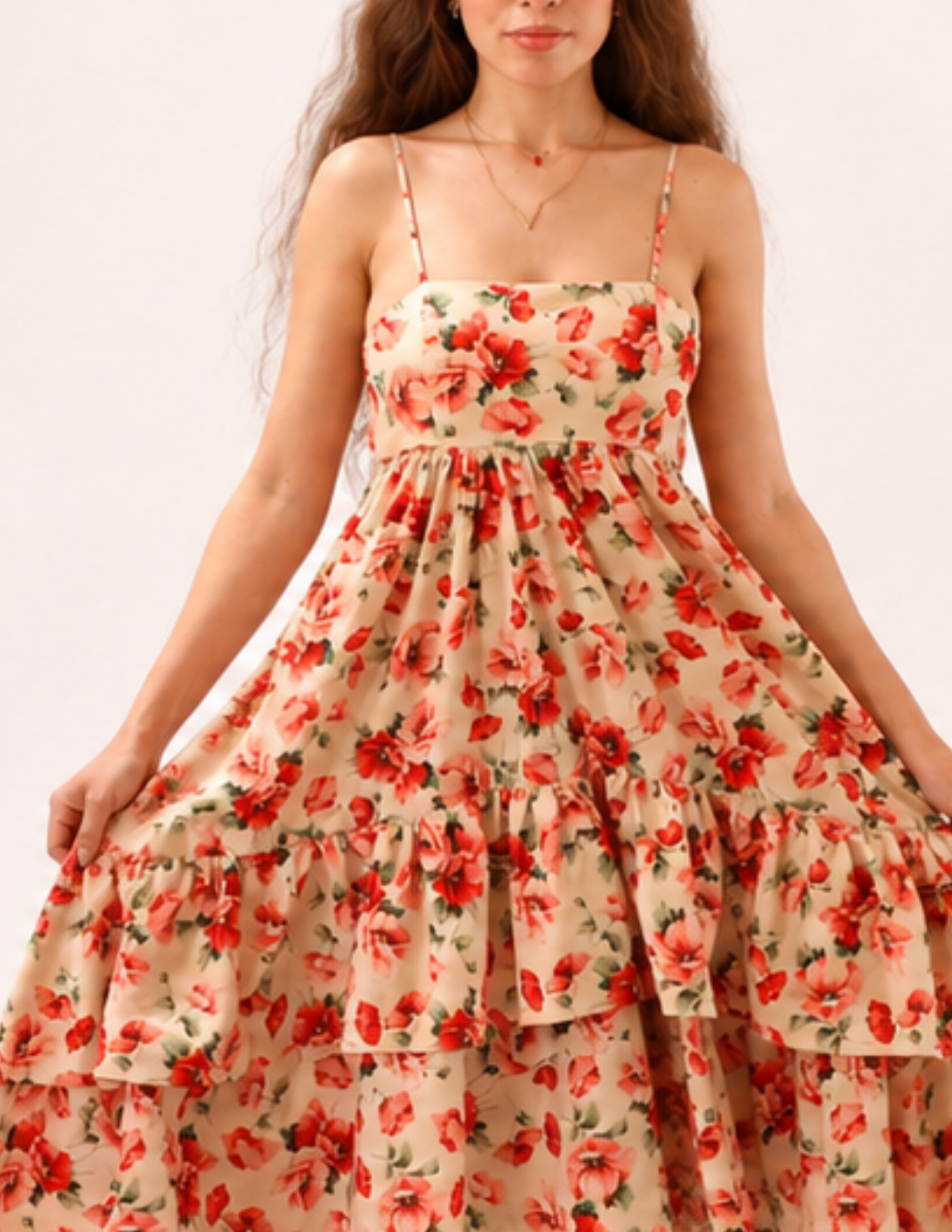 A woman wearing a beige spaghetti-strap maxi dress with a red and orange floral print, shown against a plain light background.