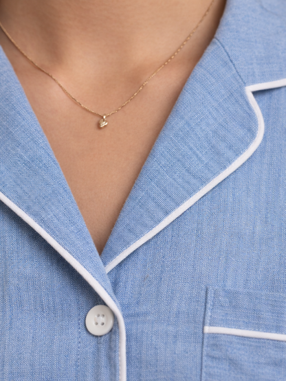 Close-up of a person wearing a light blue pajama top with white piping trim and a delicate gold necklace.