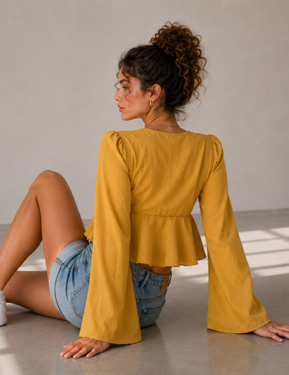 Back view of the MARBELLA women’s peplum top sewing pattern, showing the gathered waist, flared peplum and long wide sleeves in textured mustard yellow fabric