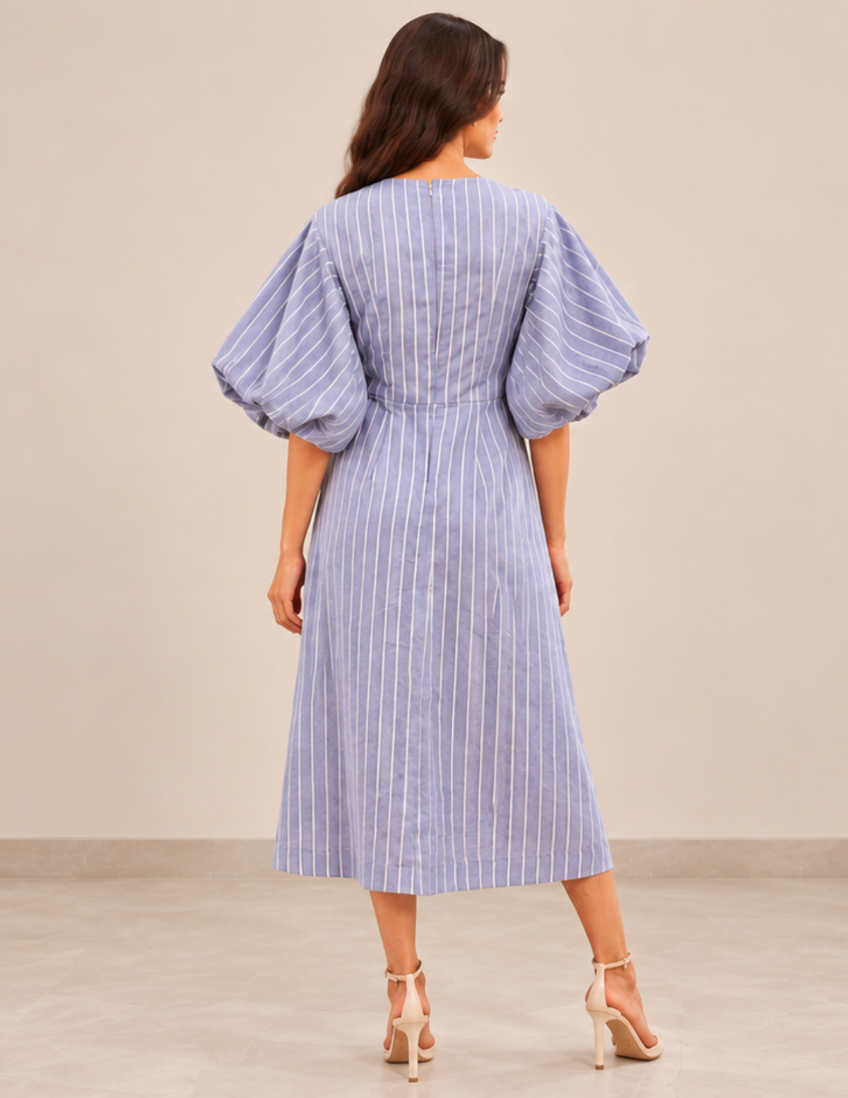 Back view of the PILAR women's midi dress sewing pattern featuring voluminous puff sleeves, a fi tted waist and a fl ared skirt in blue striped fabric