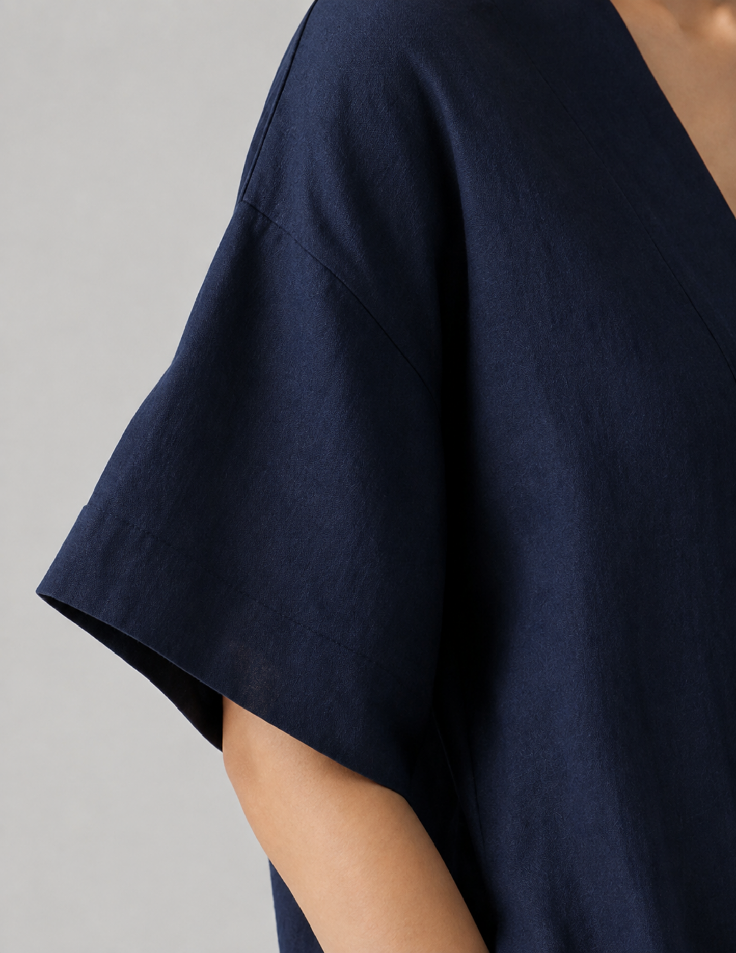 Close-up of a person wearing a loose, short-sleeve V-neck top in dark navy blue fabric against a plain light gray background.