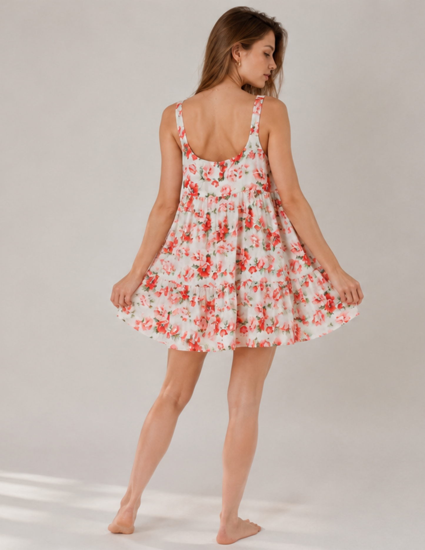 A woman modeling a sleeveless, backless mini dress with a red and orange floral pattern on a white background, shown from behind against a neutral studio backdrop.