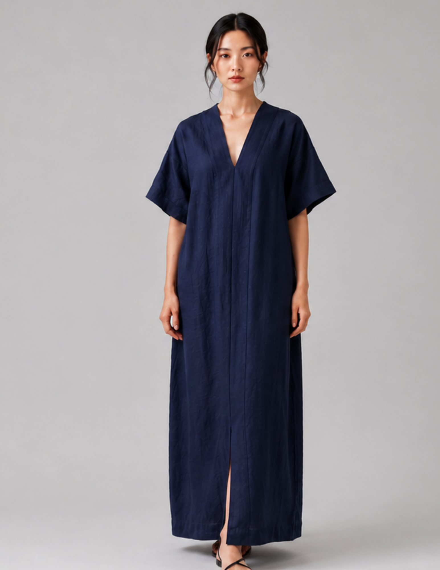 A woman modeling a navy blue, short-sleeved maxi dress with a V-neckline and front slit, photographed against a neutral gray studio background.
Women's V-neck dress sewing pattern 
shown from the front with loose fit, 
short sleeves and long straight 
silhouett
